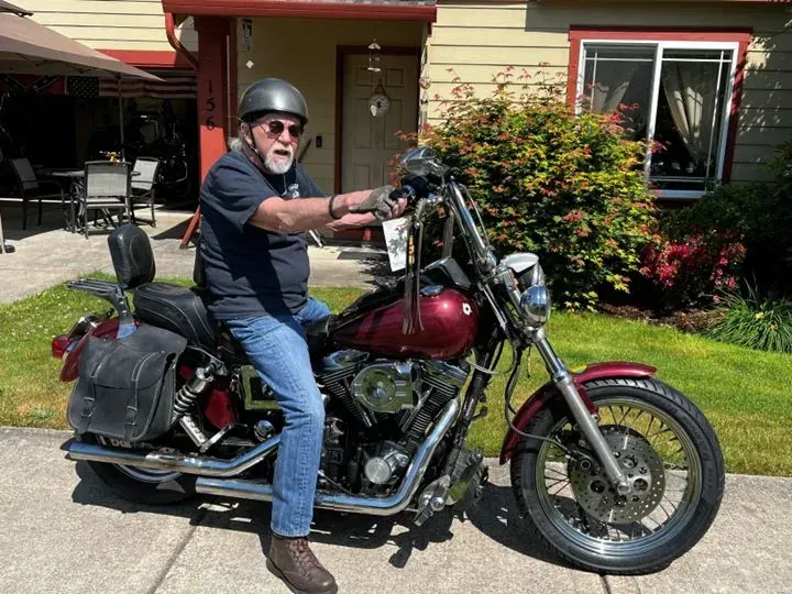 A man is sitting on a red motorcycle in front of a house.