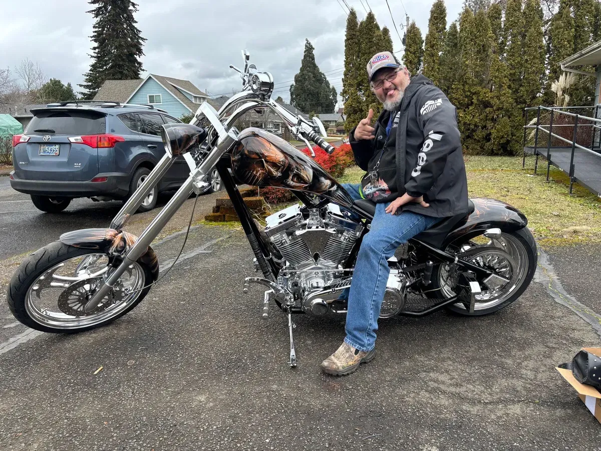 A man is sitting on a chopper motorcycle in a parking lot.