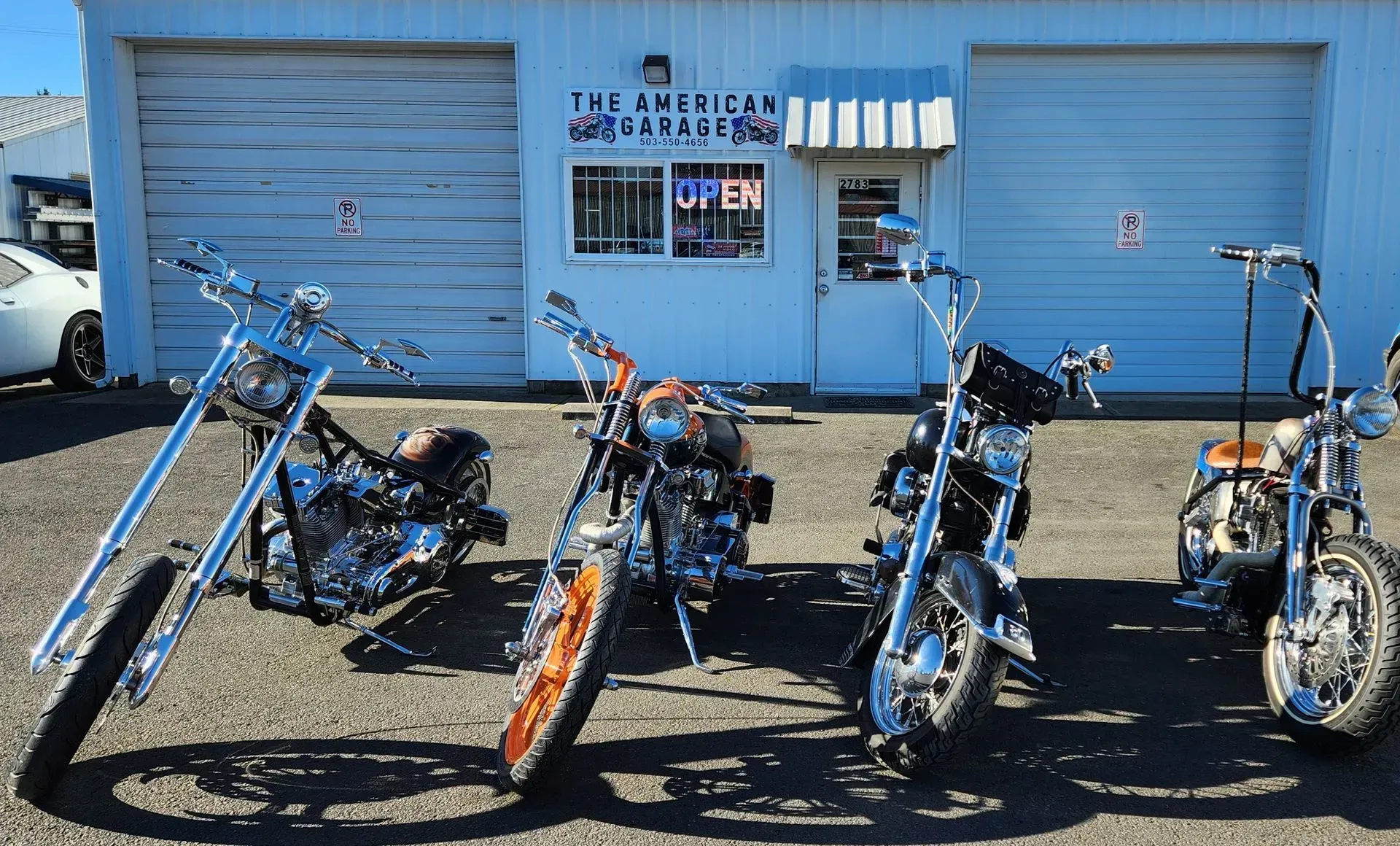 Three motorcycles are parked in front of a garage that says open