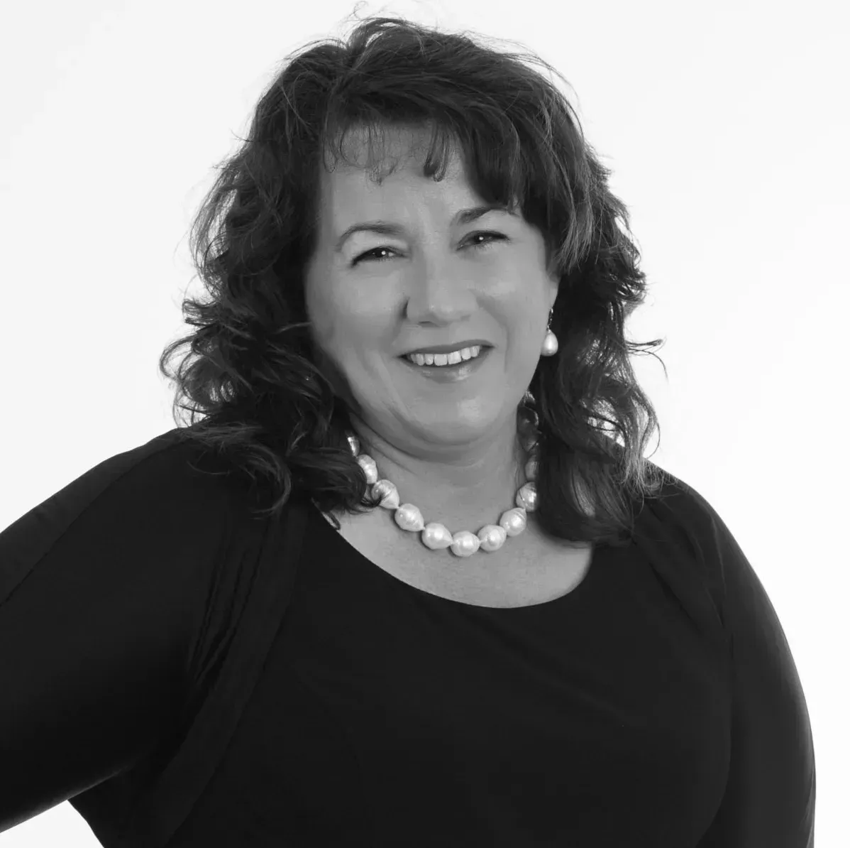 A woman wearing a black shirt and a pearl necklace is smiling in a black and white photo.