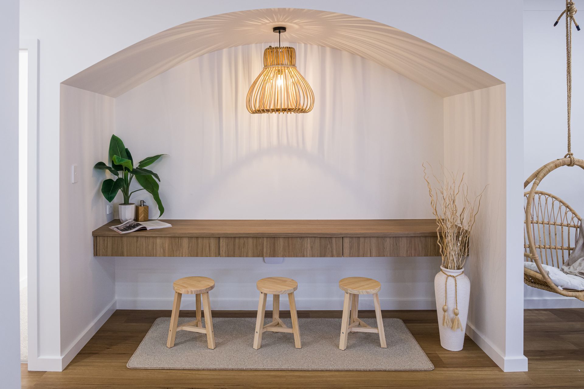 A room with a wooden desk , stools , and a hanging chair.