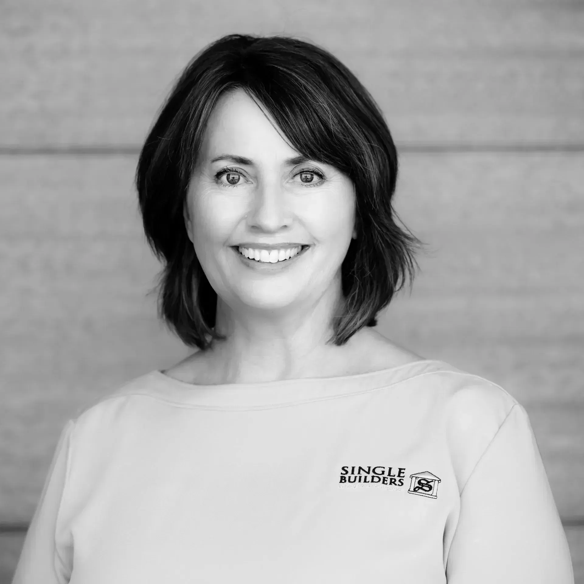 A woman in a white shirt is smiling in a black and white photo.