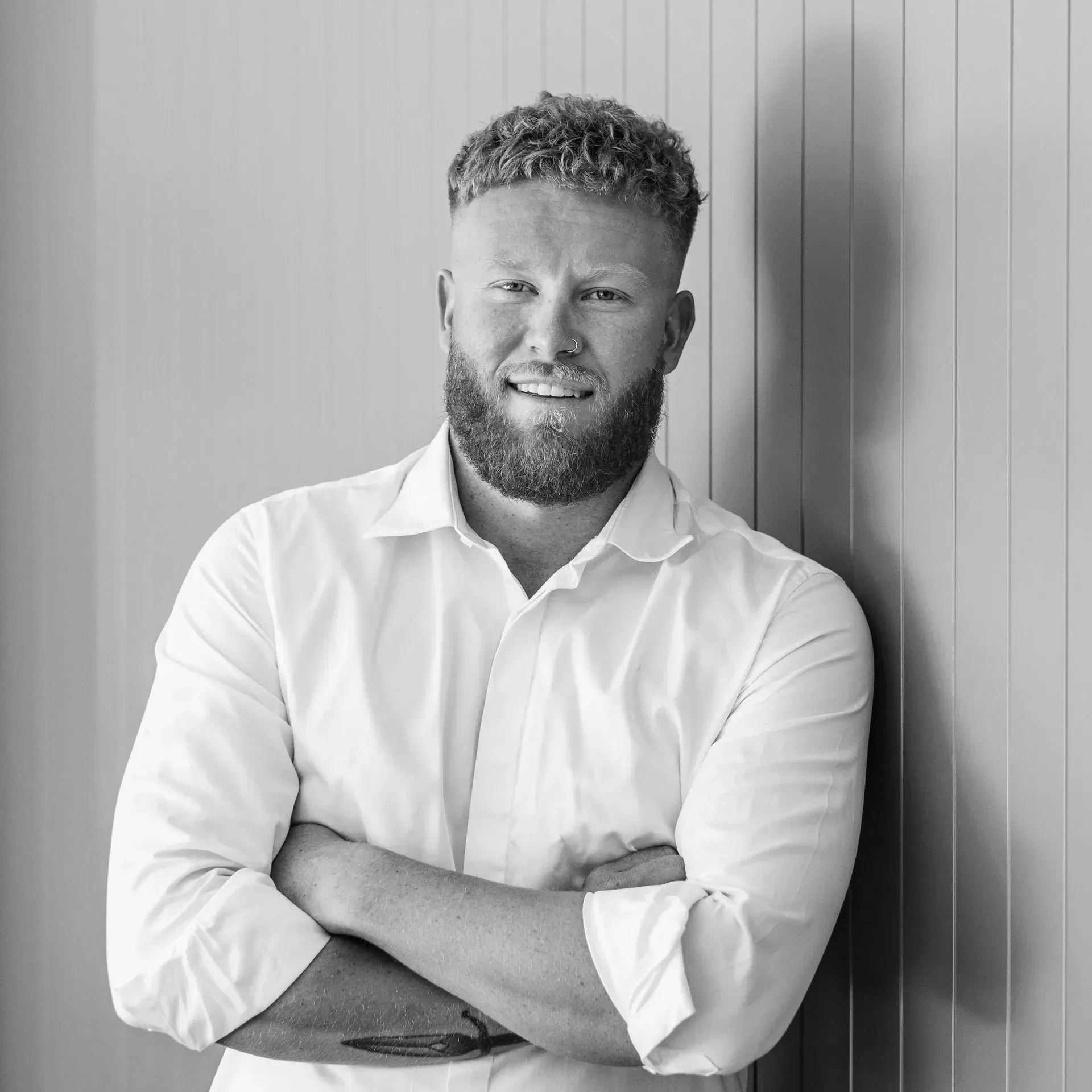 A man with a beard is standing in front of a wall with his arms crossed.