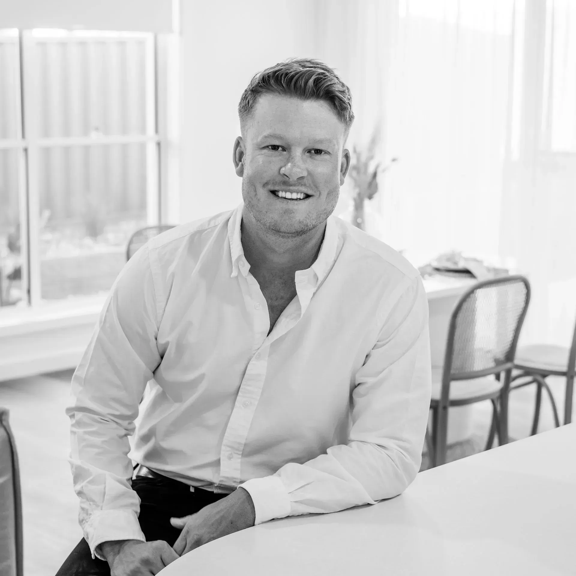 A man in a white shirt is sitting at a table in a black and white photo.
