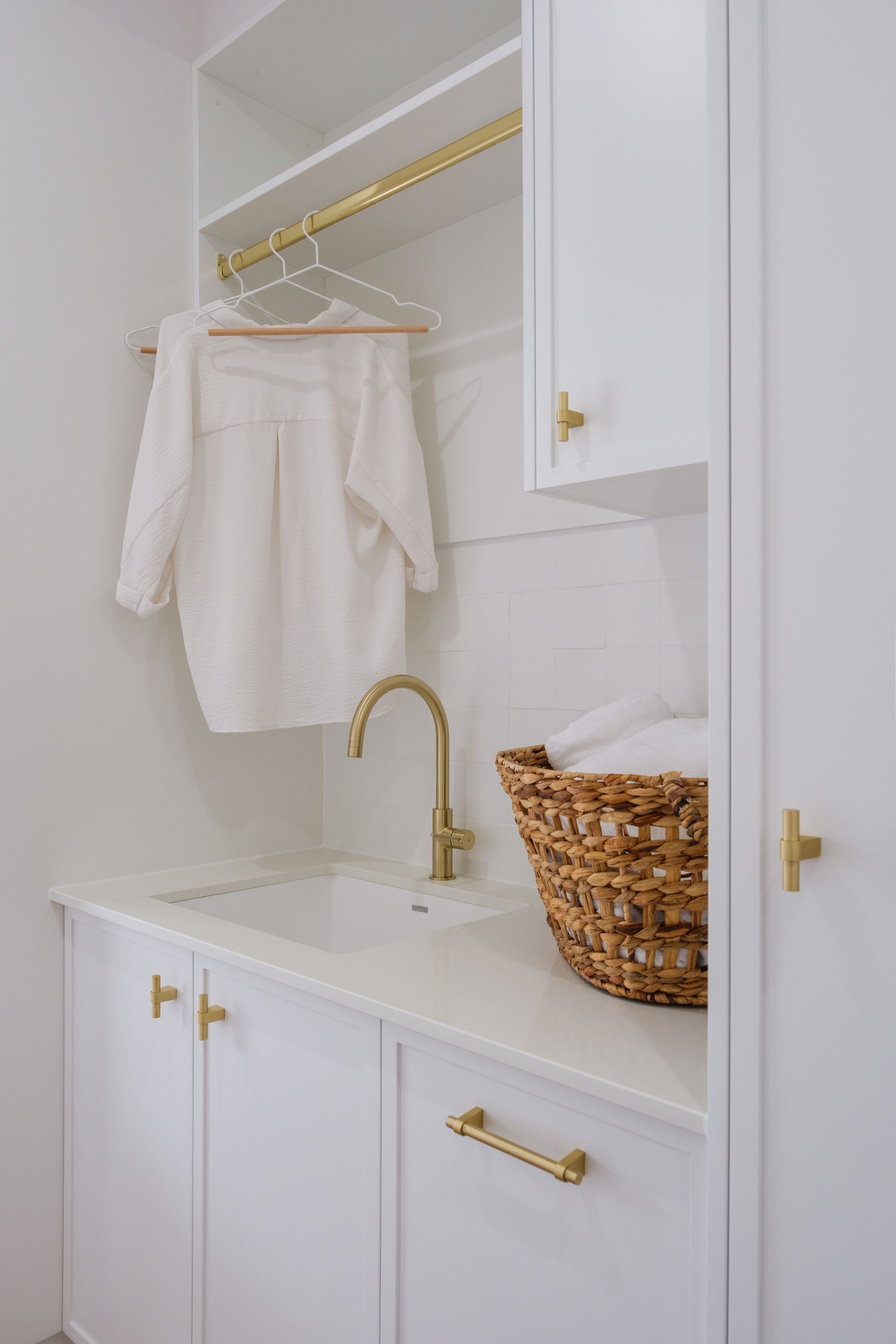 A laundry room with white cabinets , a sink , and a wicker basket.