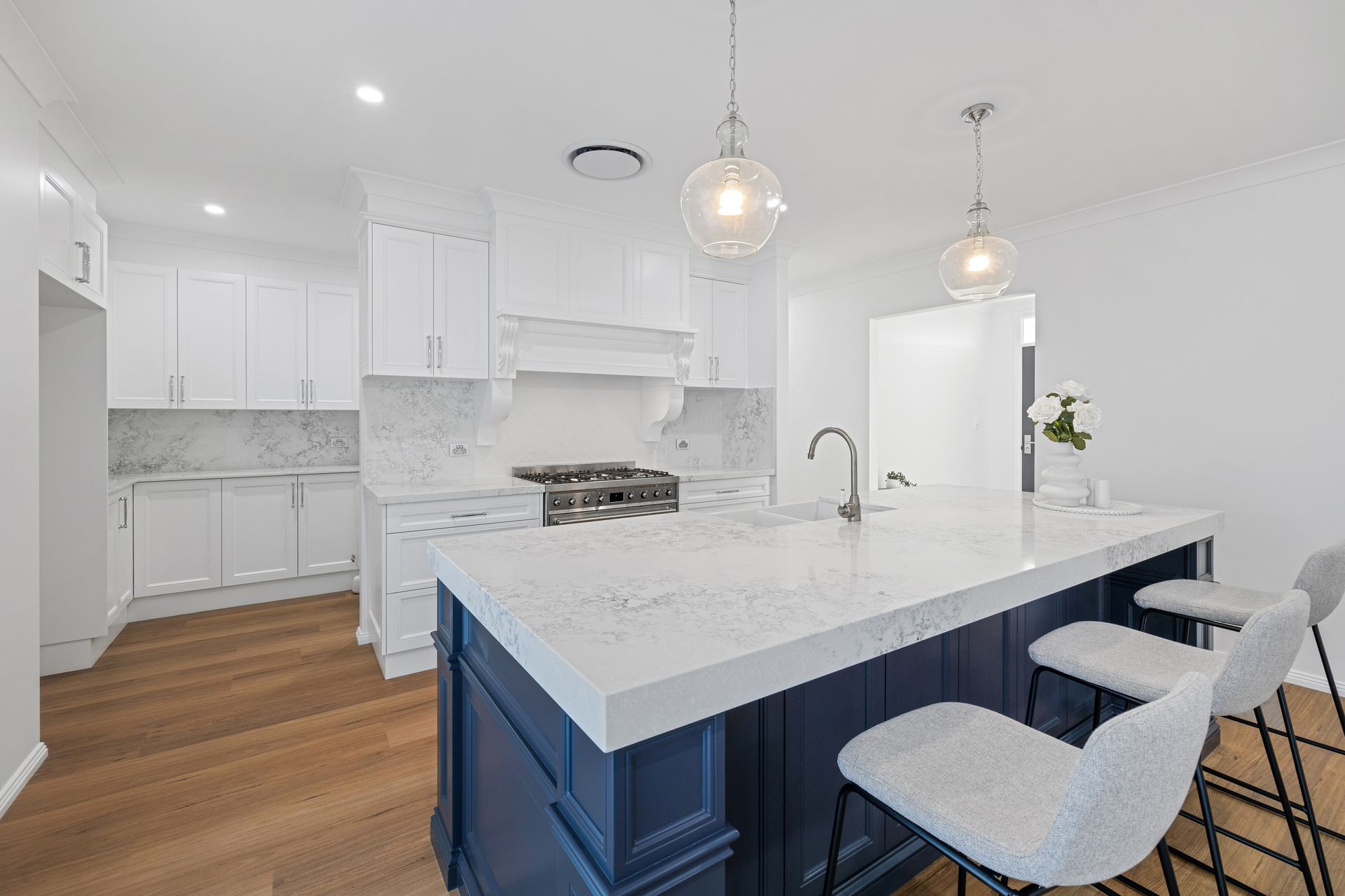 A kitchen with a blue island , white counter tops , white cabinets and wooden floors.