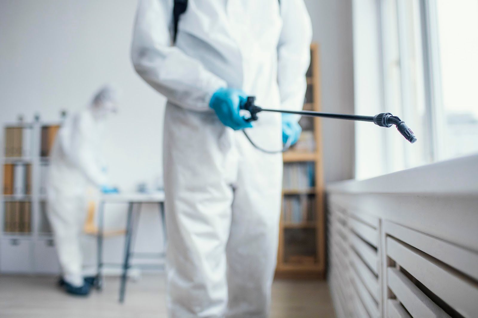 Two people in white protective suits spraying disinfectant in an office.