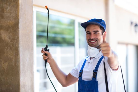 a man spraying a wall with a sprayer and giving a thumbs up