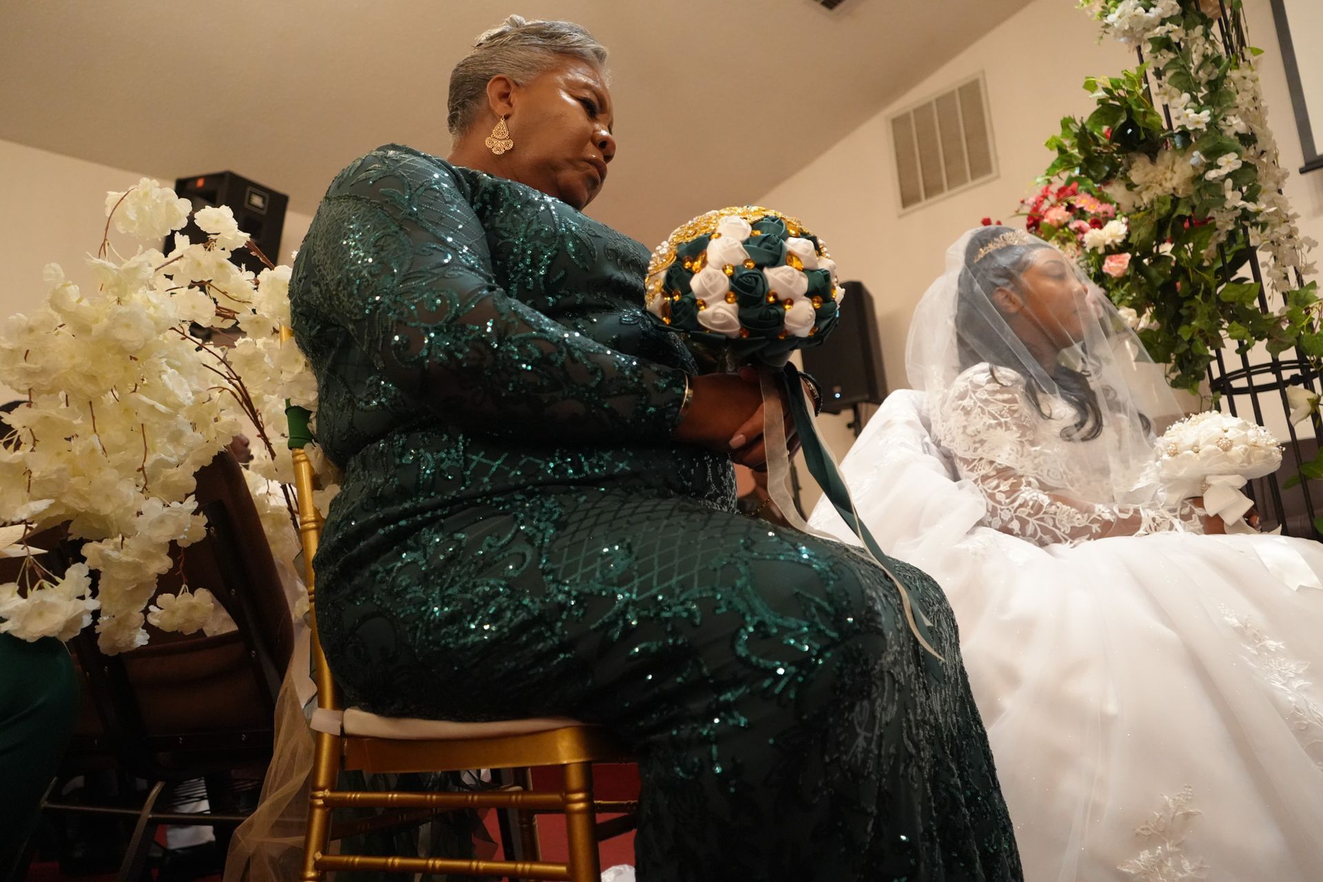 A woman in a green dress is sitting next to a bride in a white dress.