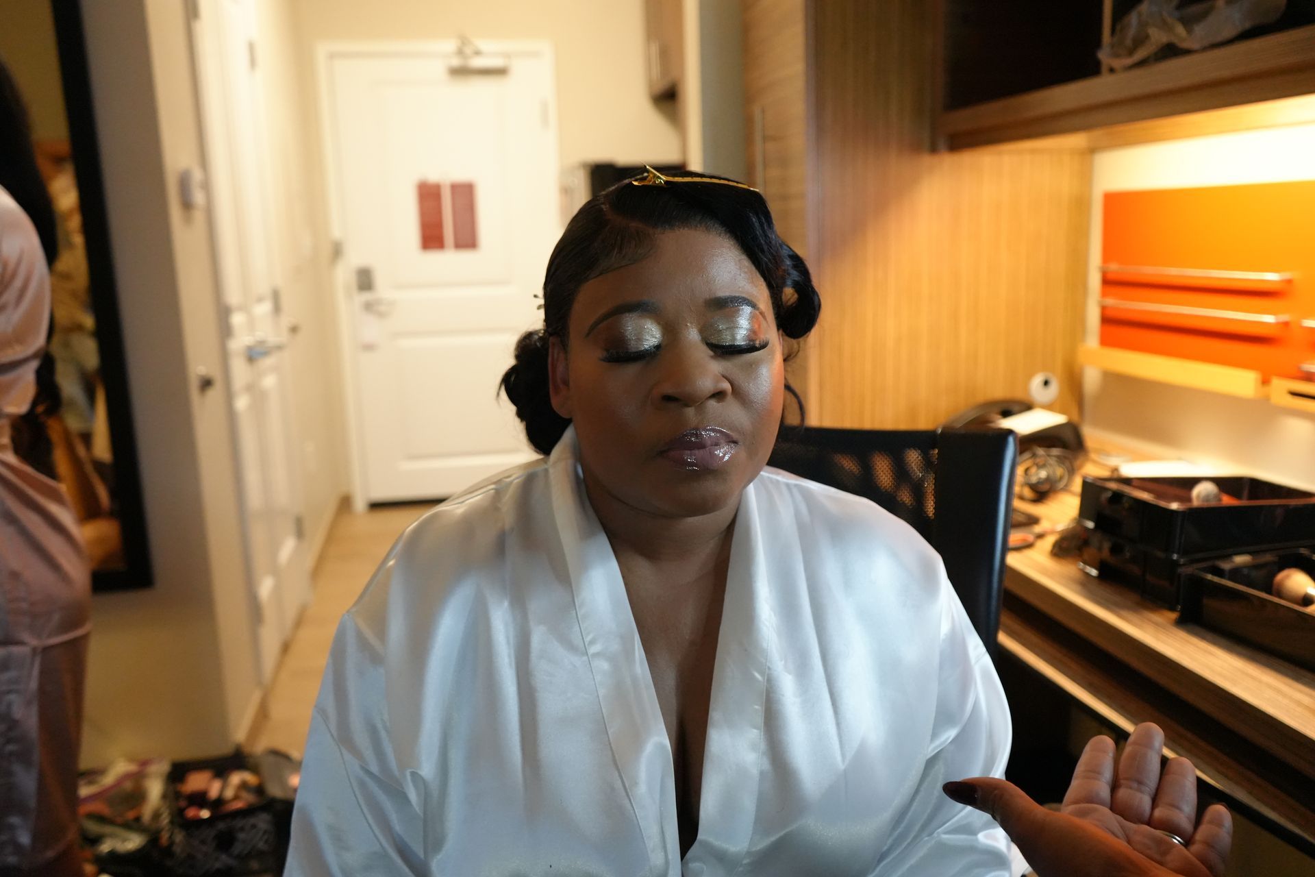 A woman is getting her makeup done in a hotel room.