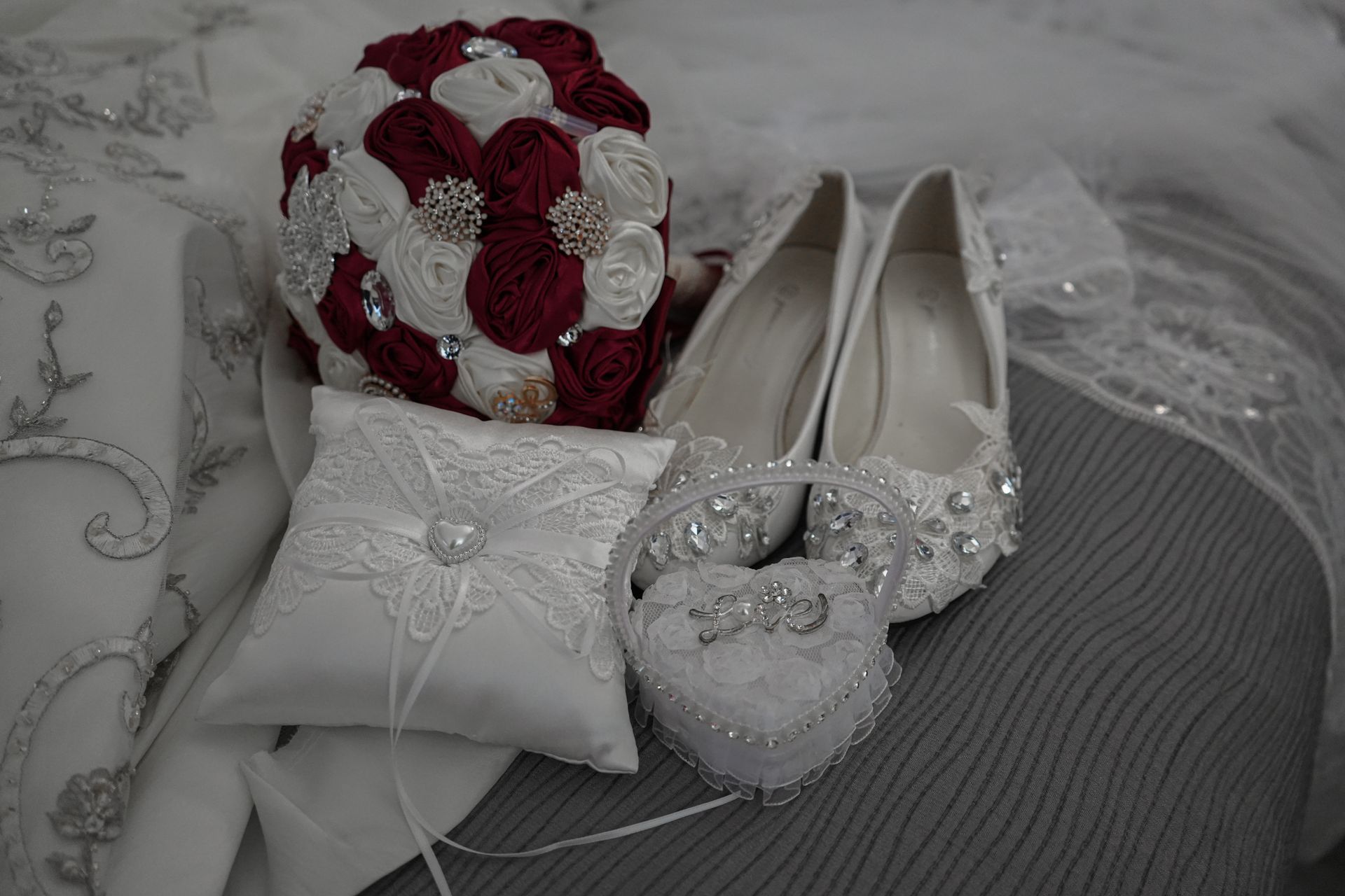 A bride 's wedding shoes , rings , and bouquet are on a bed.