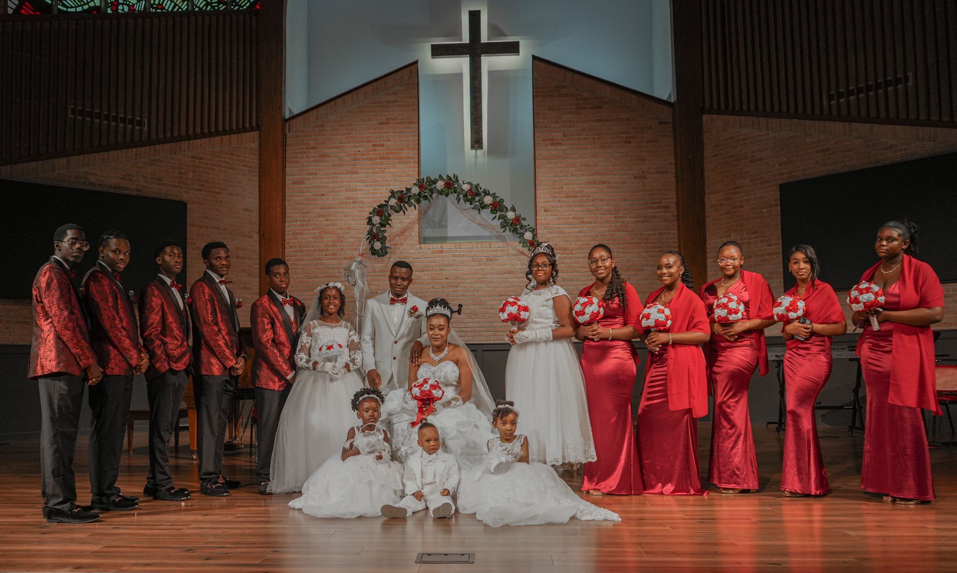 The bride and groom are posing for a picture with their wedding party in front of a cross.