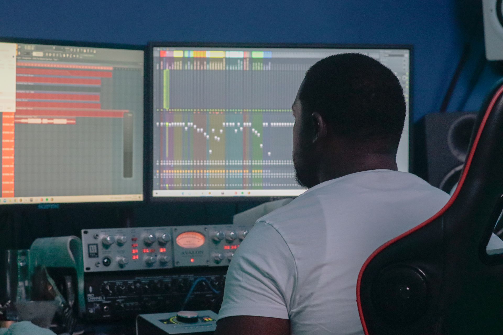 A man is sitting in front of two computer monitors in a recording studio.