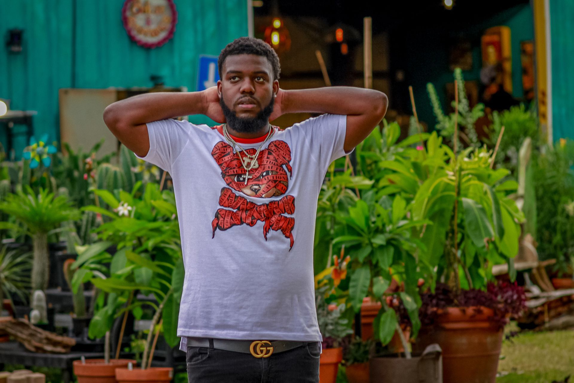 A man with his hands behind his head is standing in front of a bunch of potted plants.