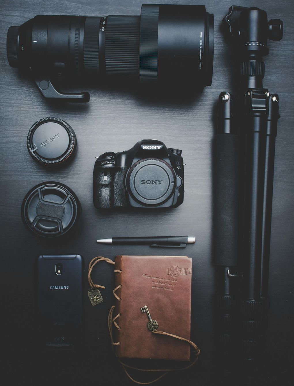 A camera lens a tripod and a notebook on a table