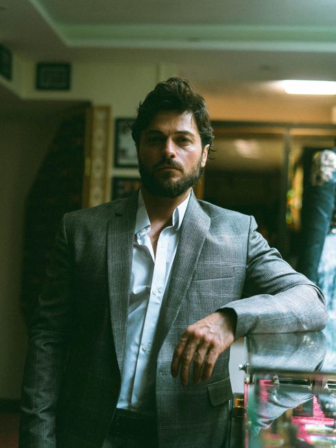 A man in a suit and white shirt is leaning against a wall.