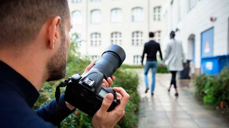 Un hombre está tomando una fotografía de una pareja caminando por una acera con una cámara.