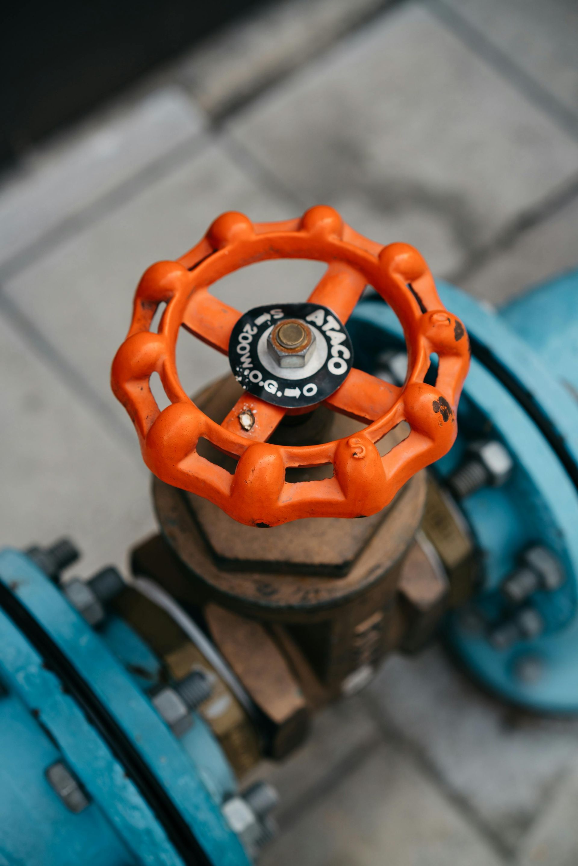 Orange valve wheel on a blue industrial pipe outdoors, seen from above.