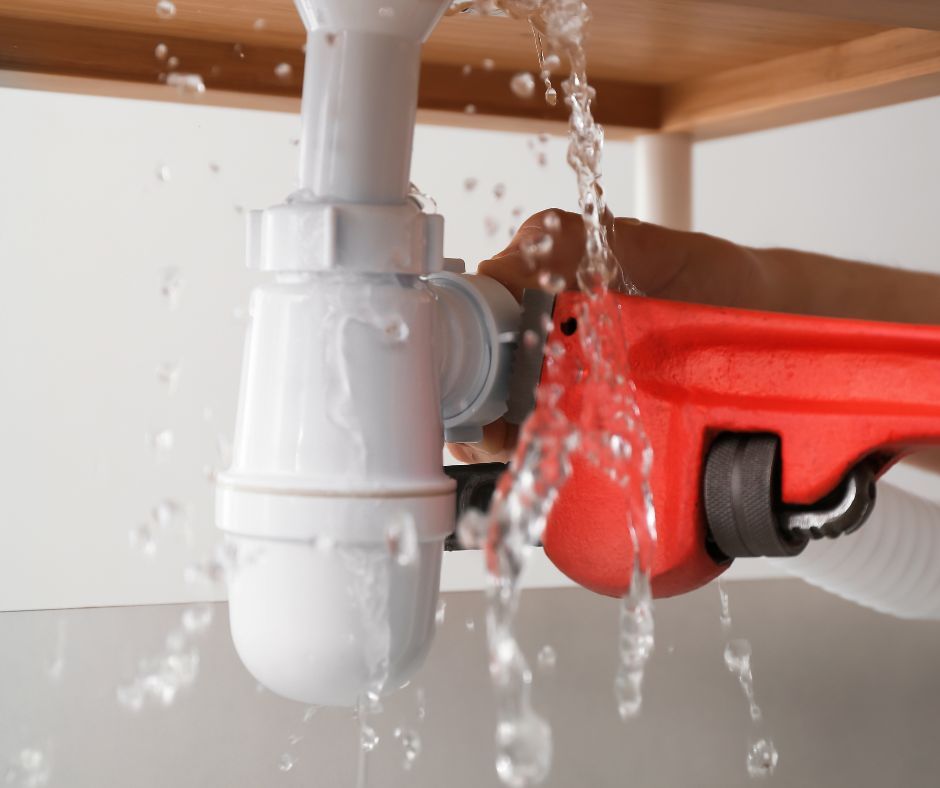 A person is fixing a sink pipe with a wrench.