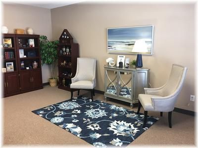 Comfortable cremation lounge with soft seating, decorative cabinet, framed wall art, and calming interior design