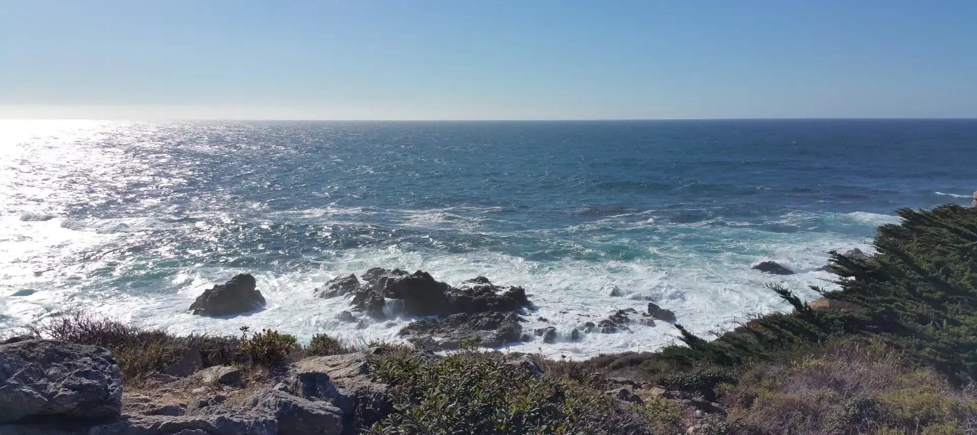 A view of the ocean from a cliff on a sunny day.