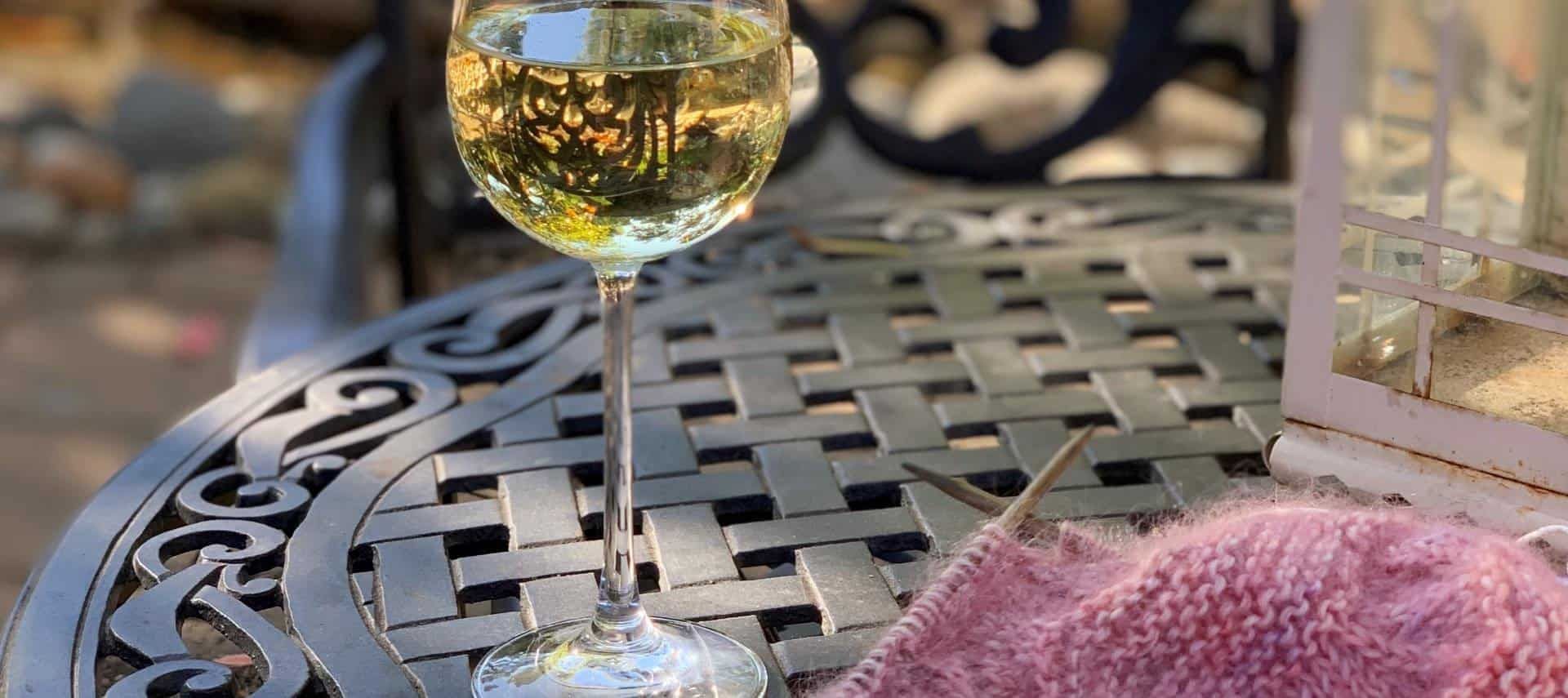 A glass of wine is sitting on a table next to a knitting project.