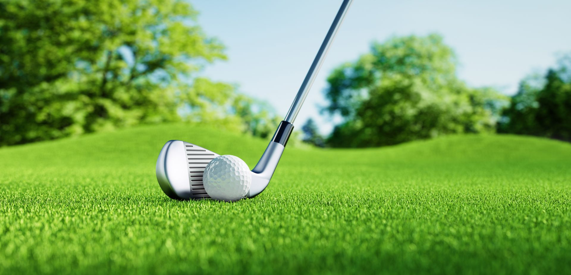 Golf club and ball on green grass, with trees and blue sky in the background.
