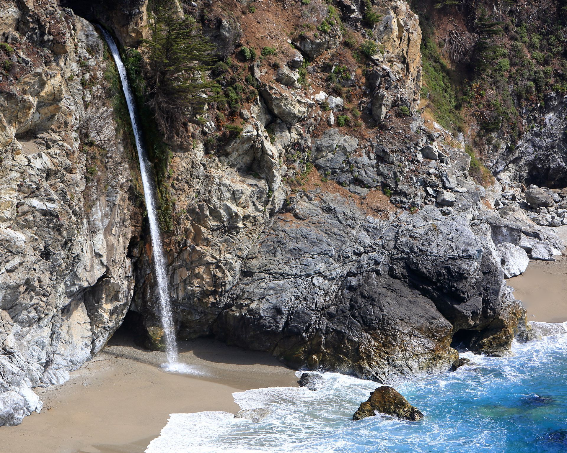 A waterfall is coming down a cliff into the ocean