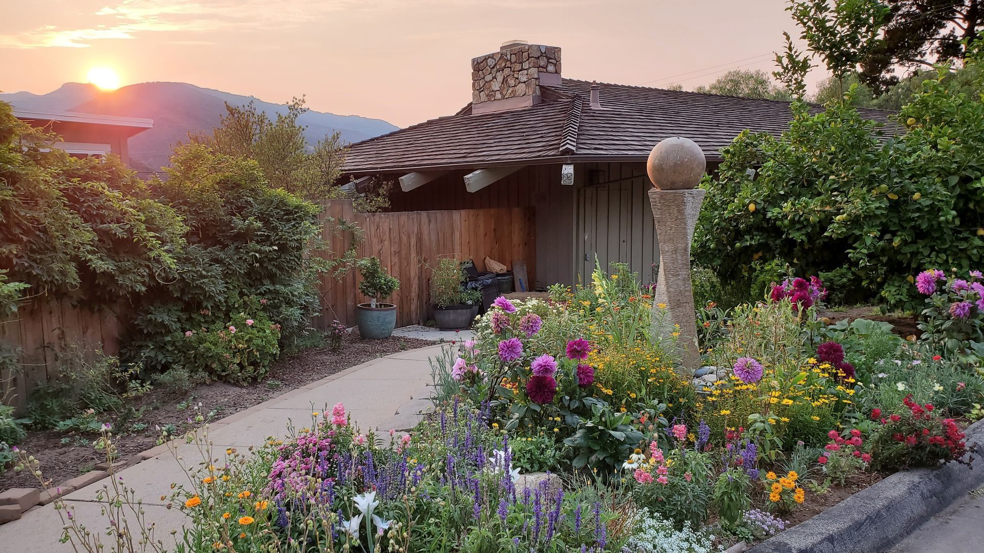 A house with flowers in front of it and a sunset in the background.