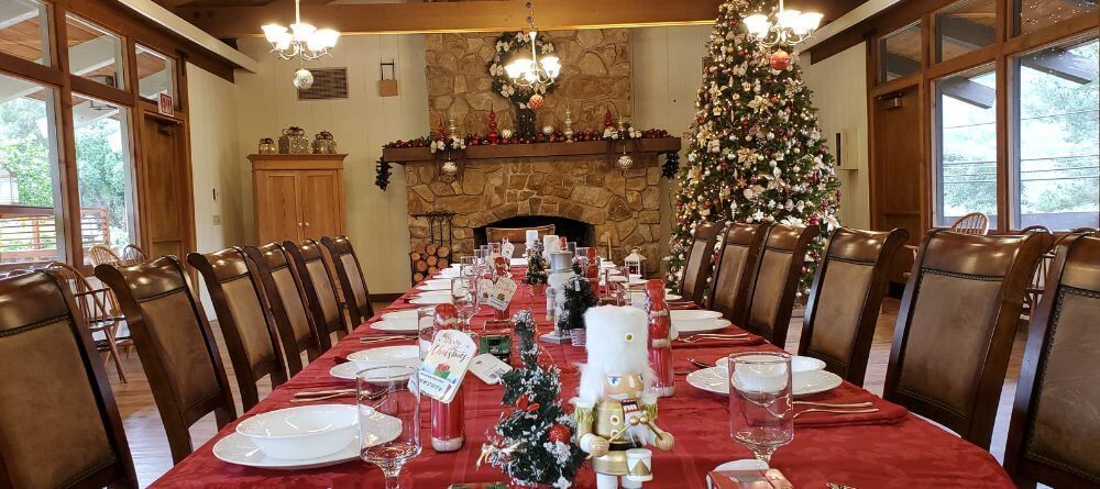 A long table with plates , glasses , and a christmas tree in the background.