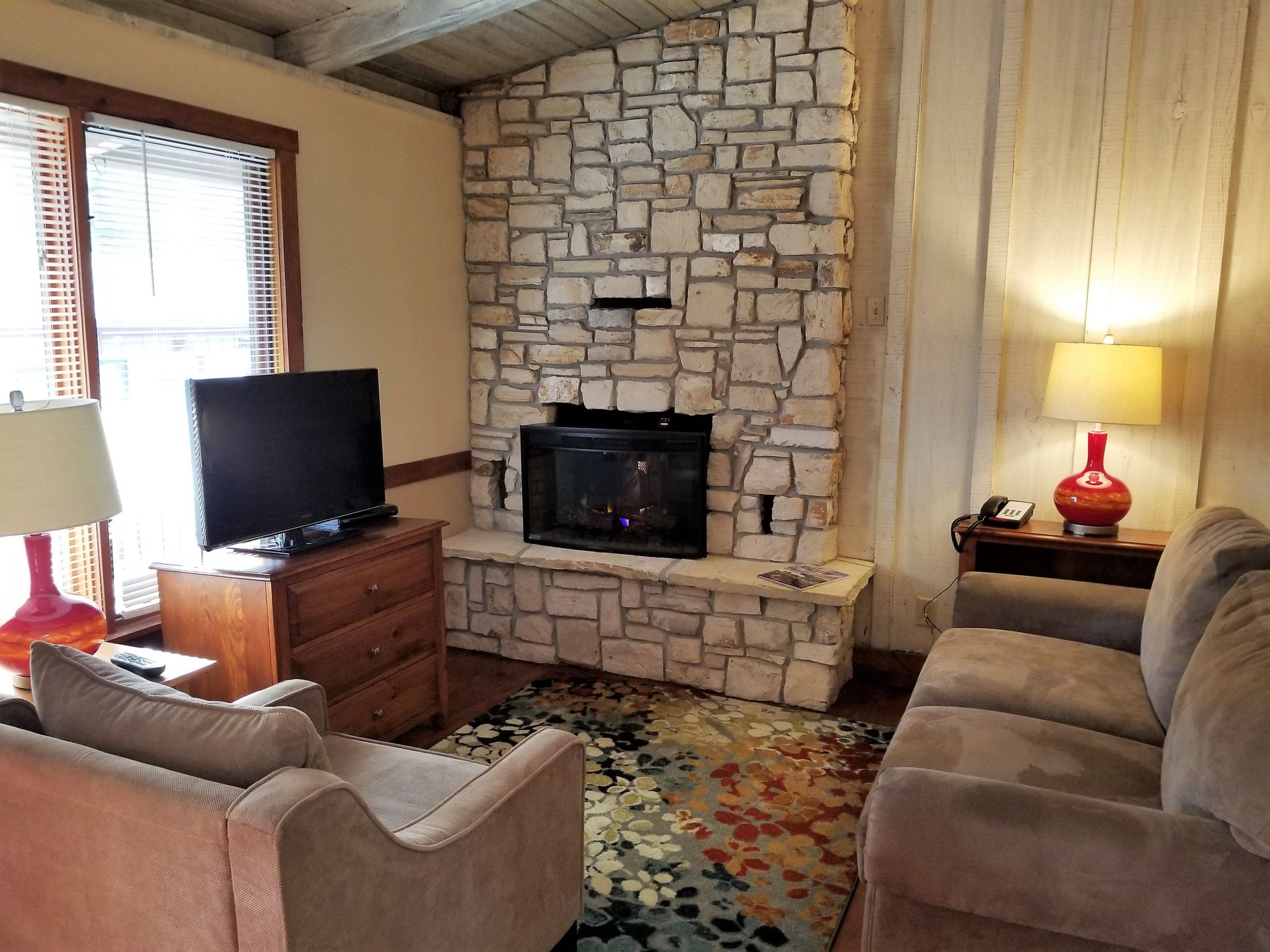 A living room with a stone fireplace and a flat screen tv