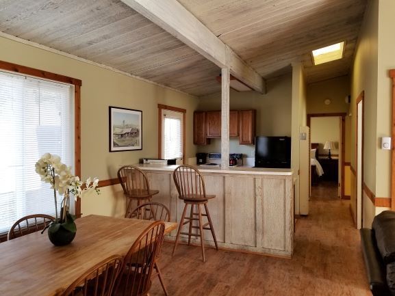 A dining room with a table and chairs and a kitchen in the background