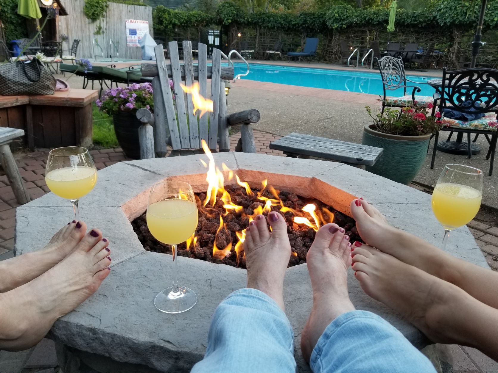 A group of people are sitting around a fire pit with drinks.