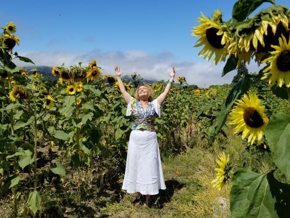 A woman is standing in a field of sunflowers with her arms outstretched.