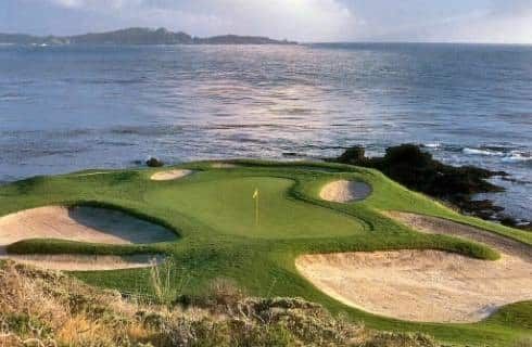 View of a hole on a golf course with multiple sand traps next to cliffs and the ocean