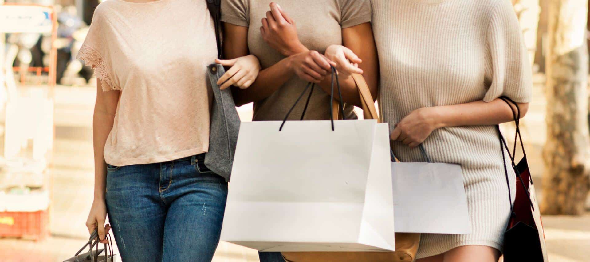 Three women are walking down the street holding shopping bags.