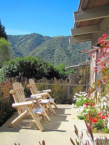 A row of wooden chairs are sitting on a patio with mountains in the background.