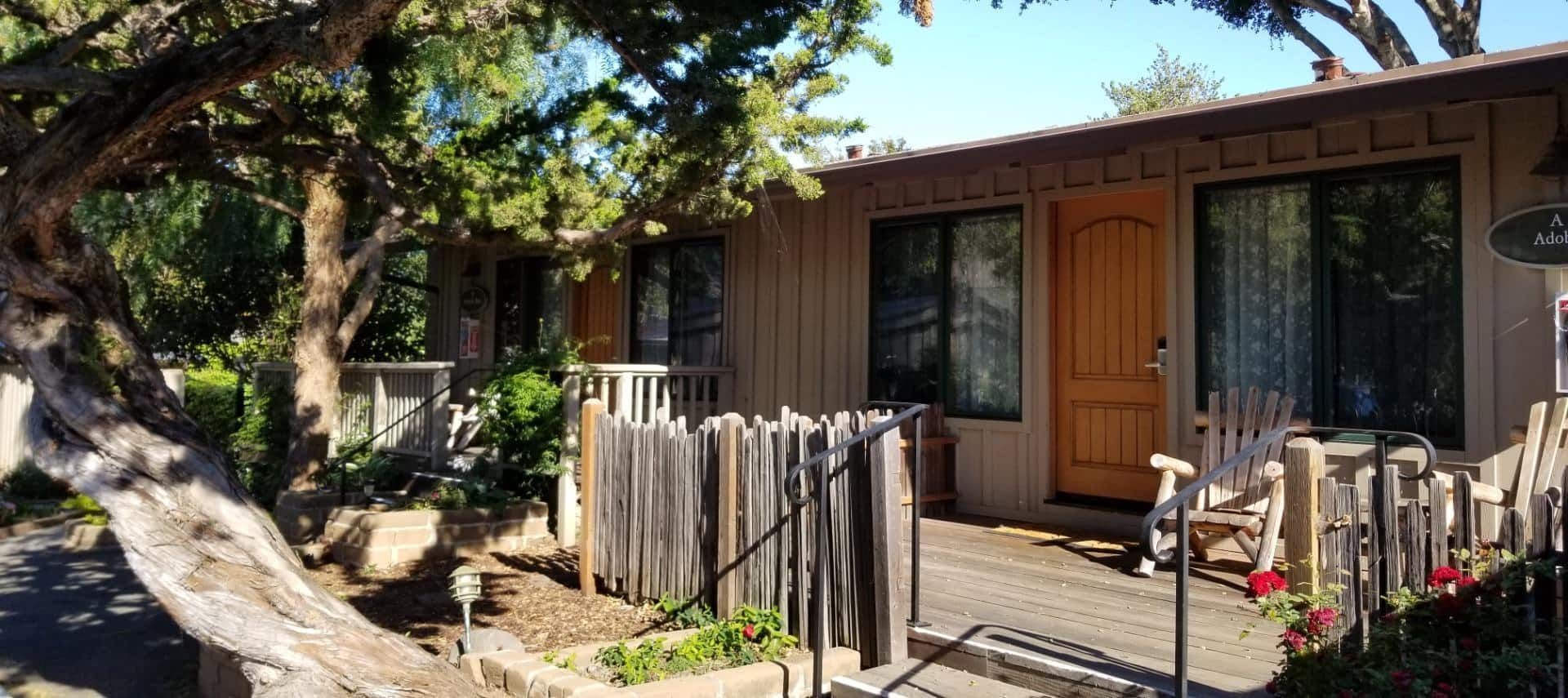 A house with a wooden fence around it and a tree in front of it.