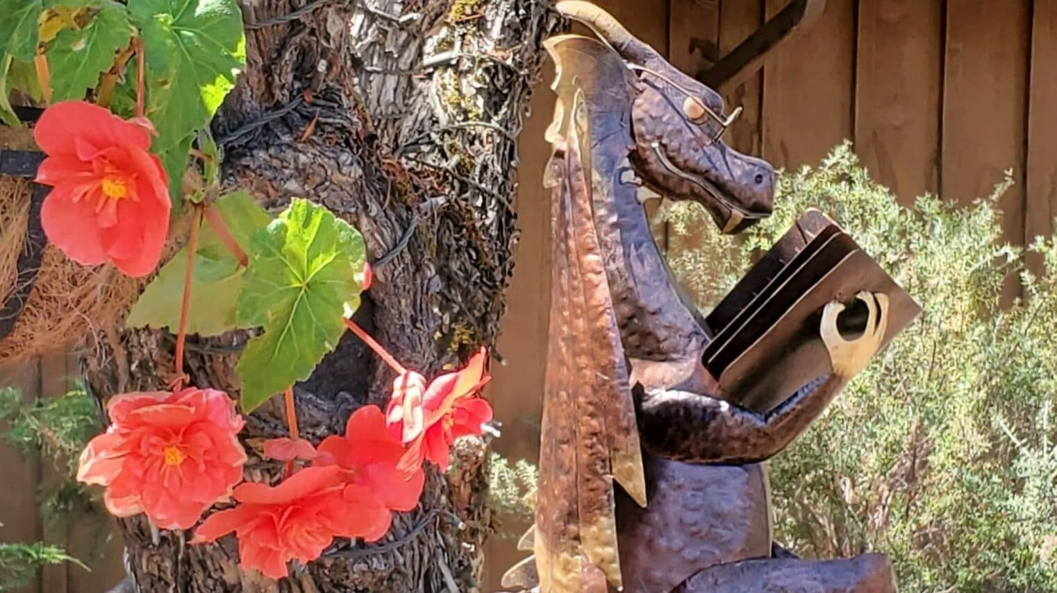 A statue of a dragon reading a book next to a tree with red flowers.