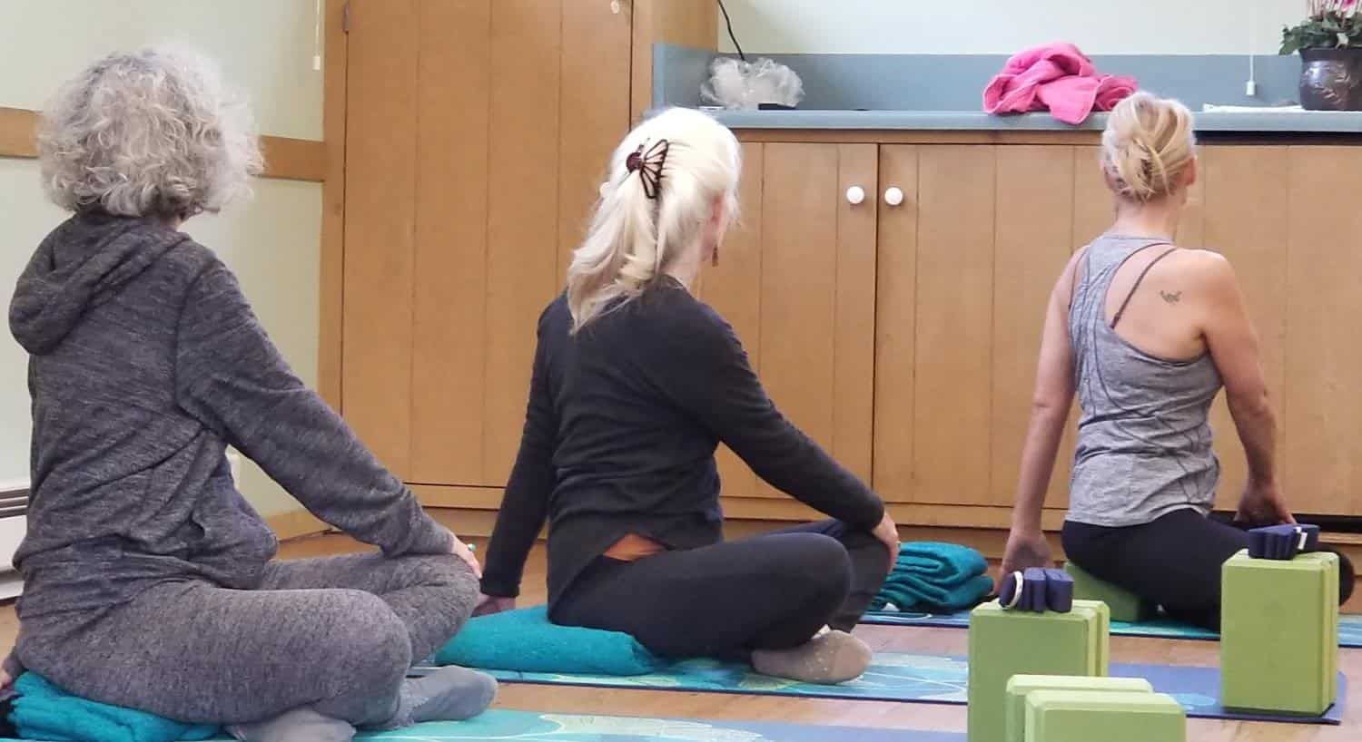 Three women are sitting on yoga mats in a room
