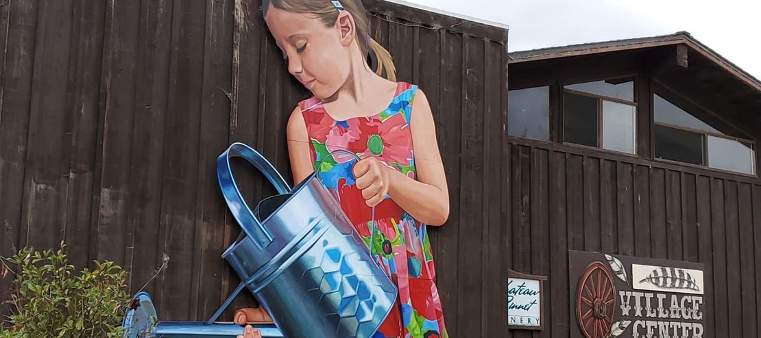 A little girl is watering a plant with a watering can.