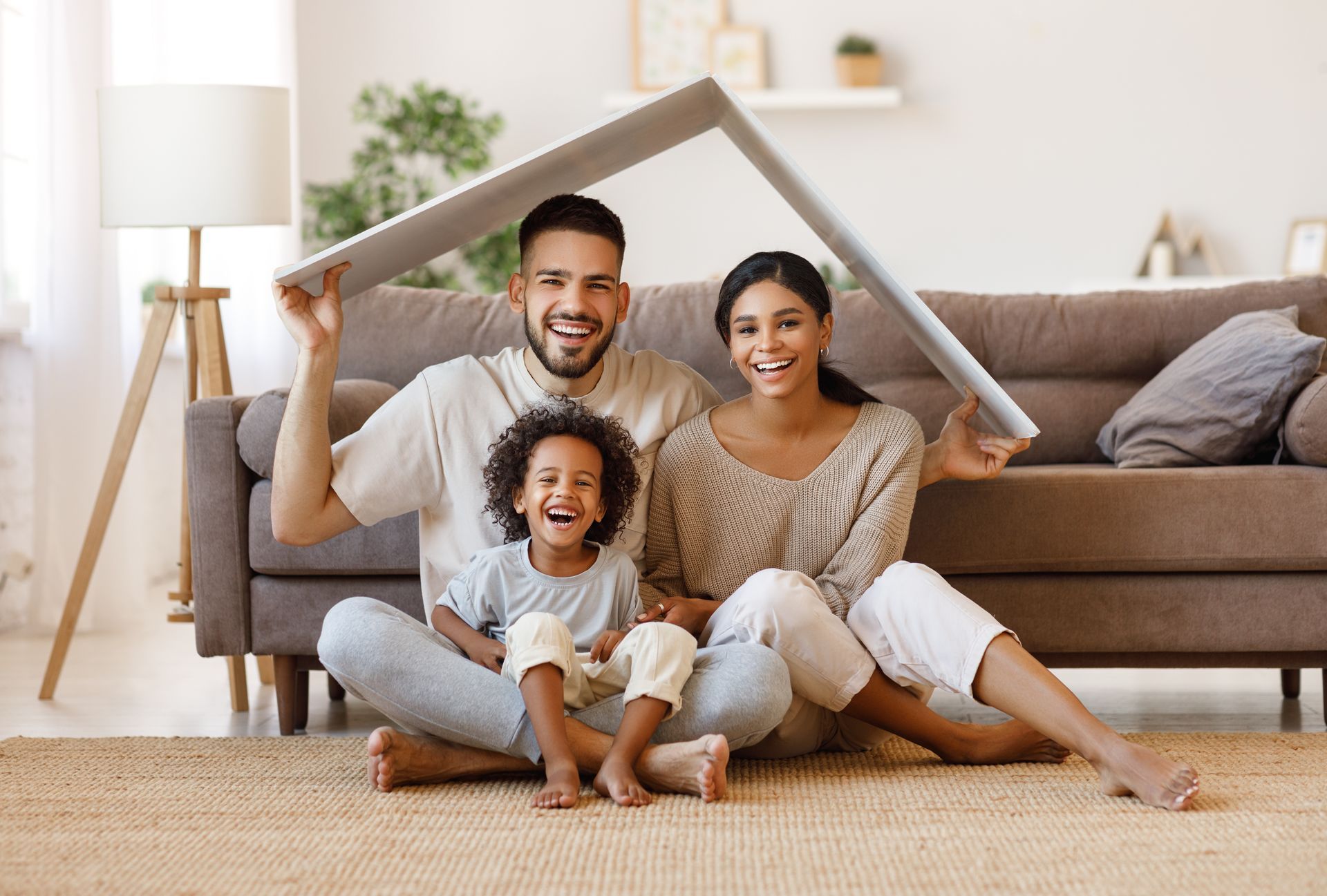 A family is sitting on the floor in a living room holding a cardboard house.