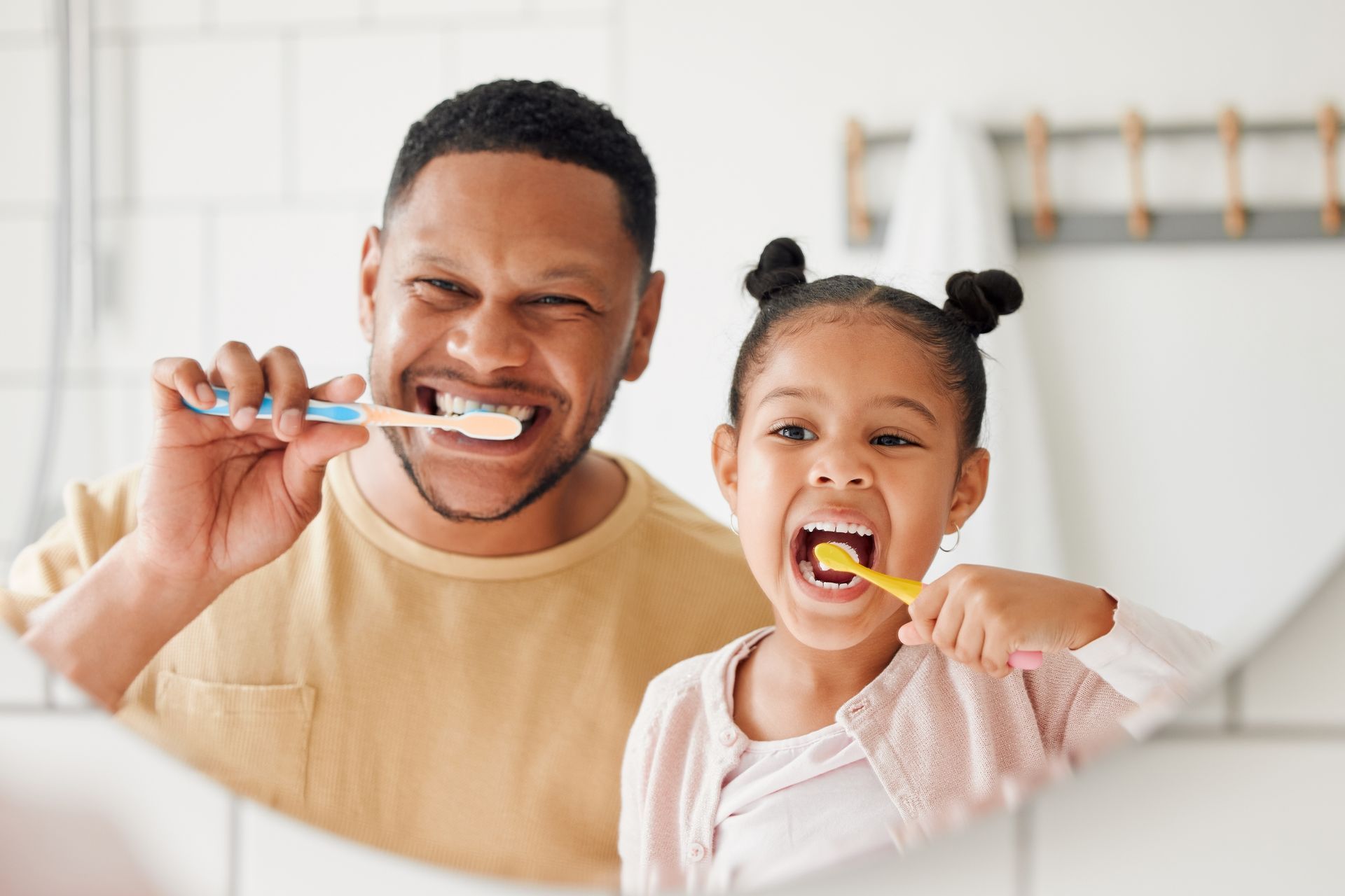 A man and a little girl are brushing their teeth in front of a mirror.