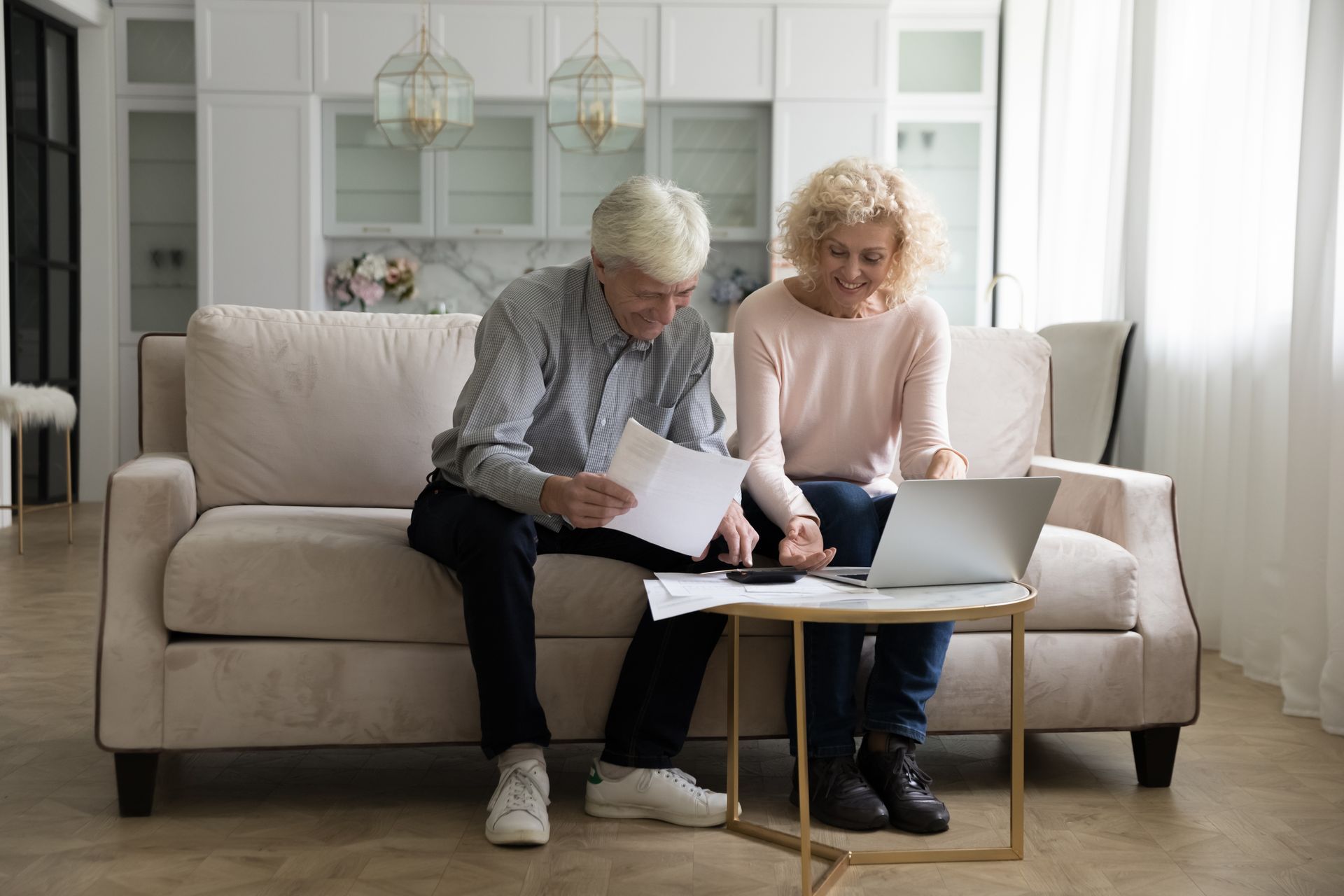 An elderly couple is sitting on a couch looking at a laptop.