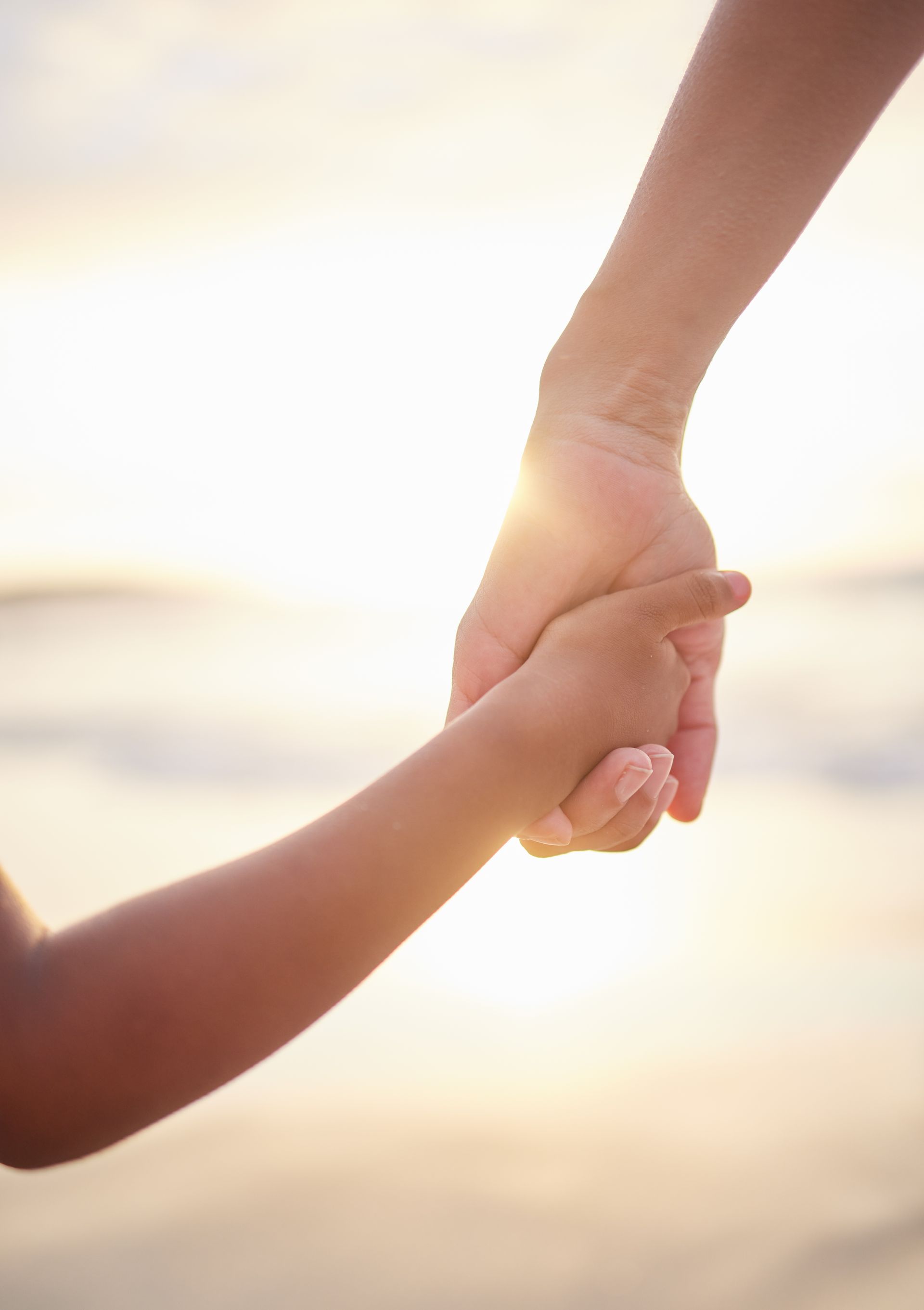 A woman and child are holding hands on the beach at sunset.