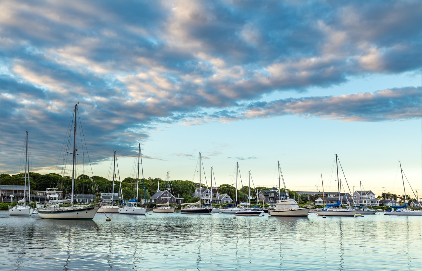 A row of sailboats are docked in a harbor on a cloudy day.