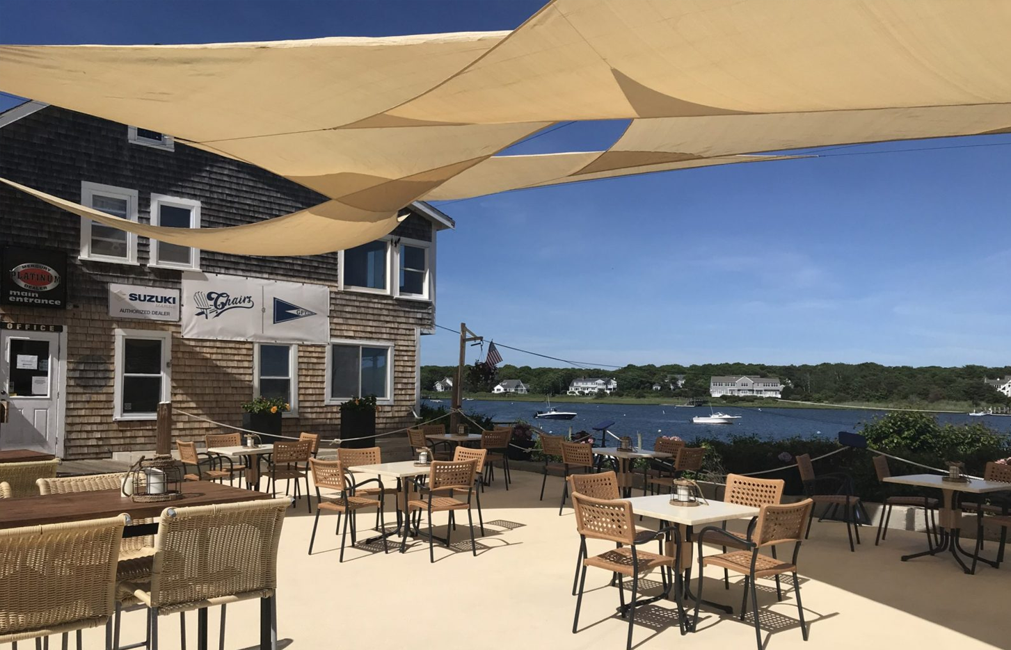 A patio with tables and chairs under umbrellas overlooking a body of water.