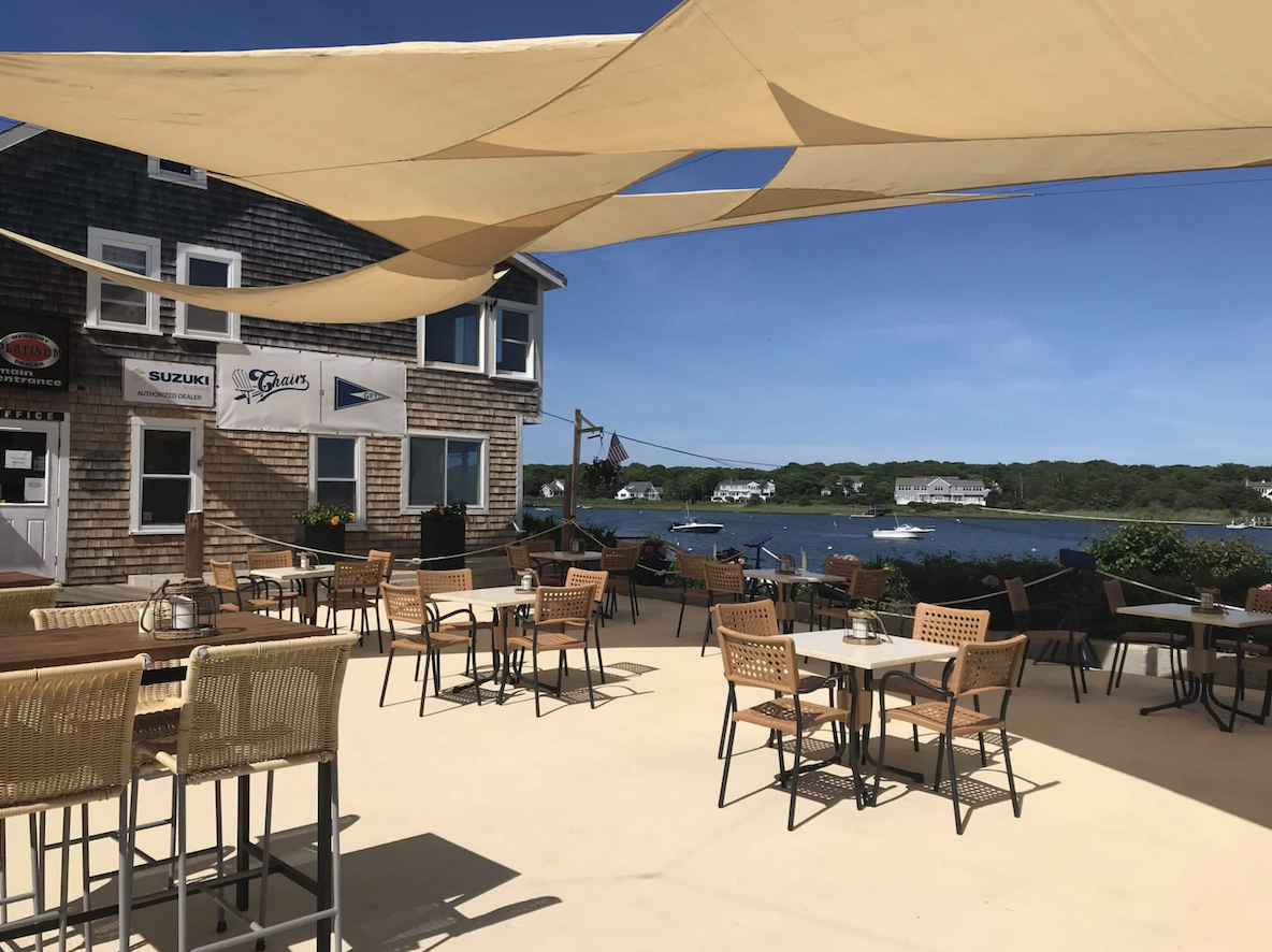 A patio with tables and chairs under umbrellas overlooking a body of water.