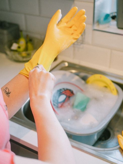 A woman wearing yellow rubber gloves is washing dishes in a kitchen sink.