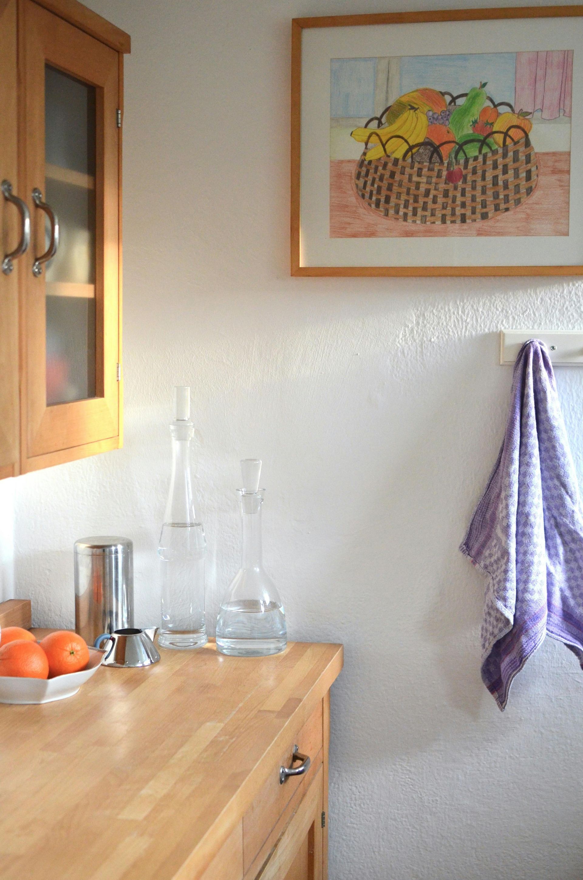 A picture of a basket of fruit hangs above a wooden counter in a kitchen.